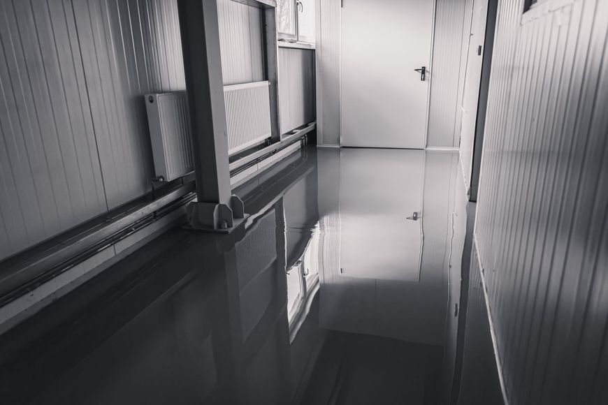 Un sol gris réfléchissant dans un couloir aux murs blancs et à la porte fermée.