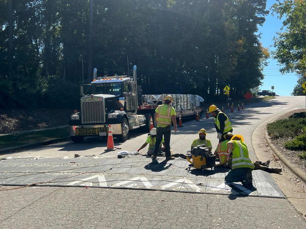 A group of construction workers are working on a road next to a semi truck.