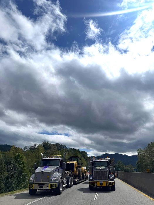 Two semi trucks are driving down a highway on a cloudy day.