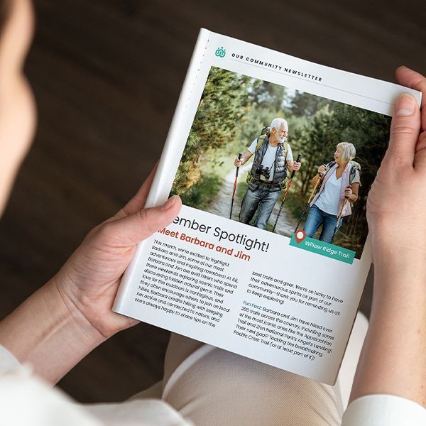 A person is holding a newsletter with a picture of a man and woman hiking on it.