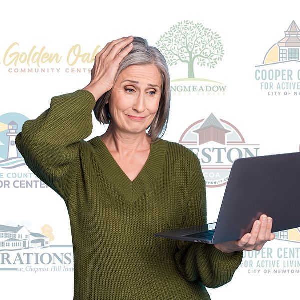 A woman in a green sweater is holding a laptop while holding her head.