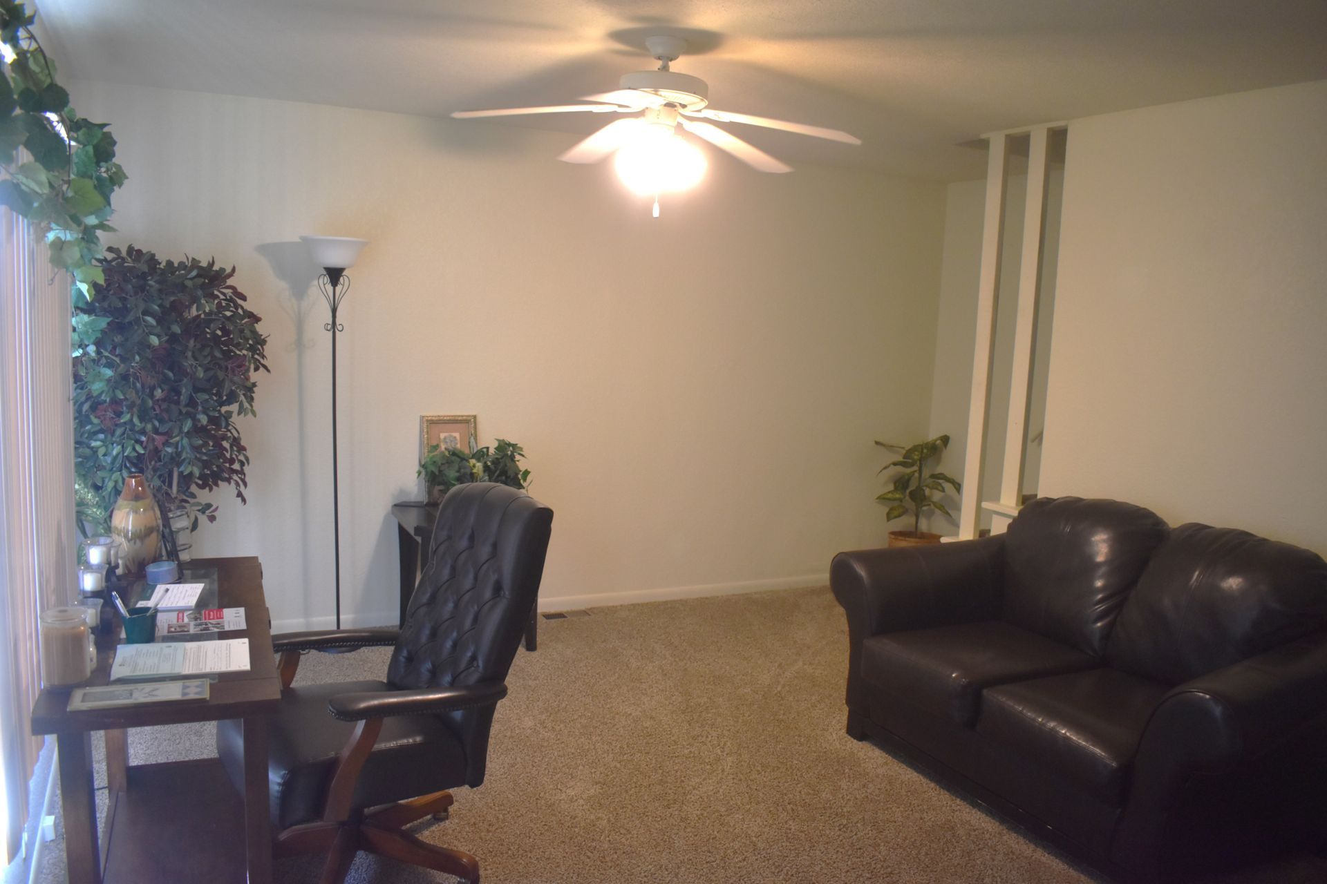 Living room with a desk, leather couch, plants, and ceiling fan.