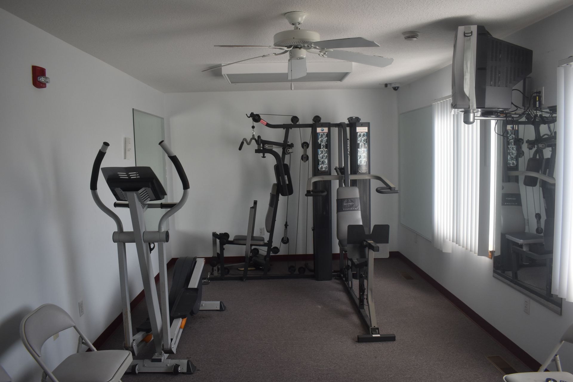 Gym with elliptical, multi-gym, television, and ceiling fan.