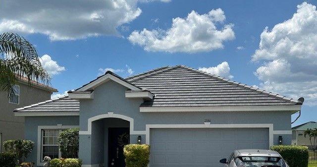 Blue house with gray roof and garage door against a cloudy sky.