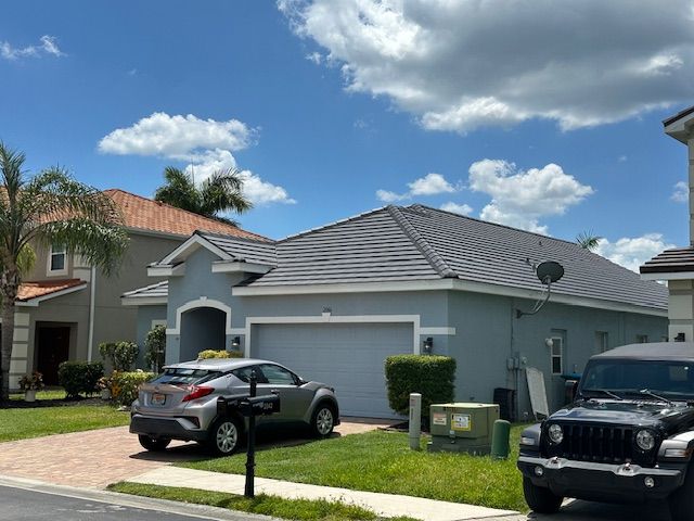 A blue house with a gray roof and a gray SUV in the driveway under a blue sky with clouds.