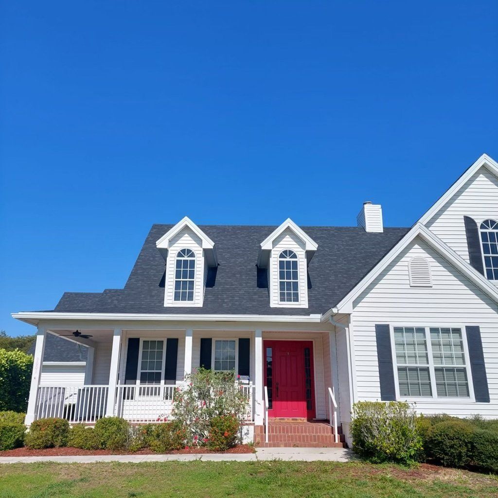 A white house with a red door, black shutters and a new roof installed by Four Peaks Roofing in Fort Myers