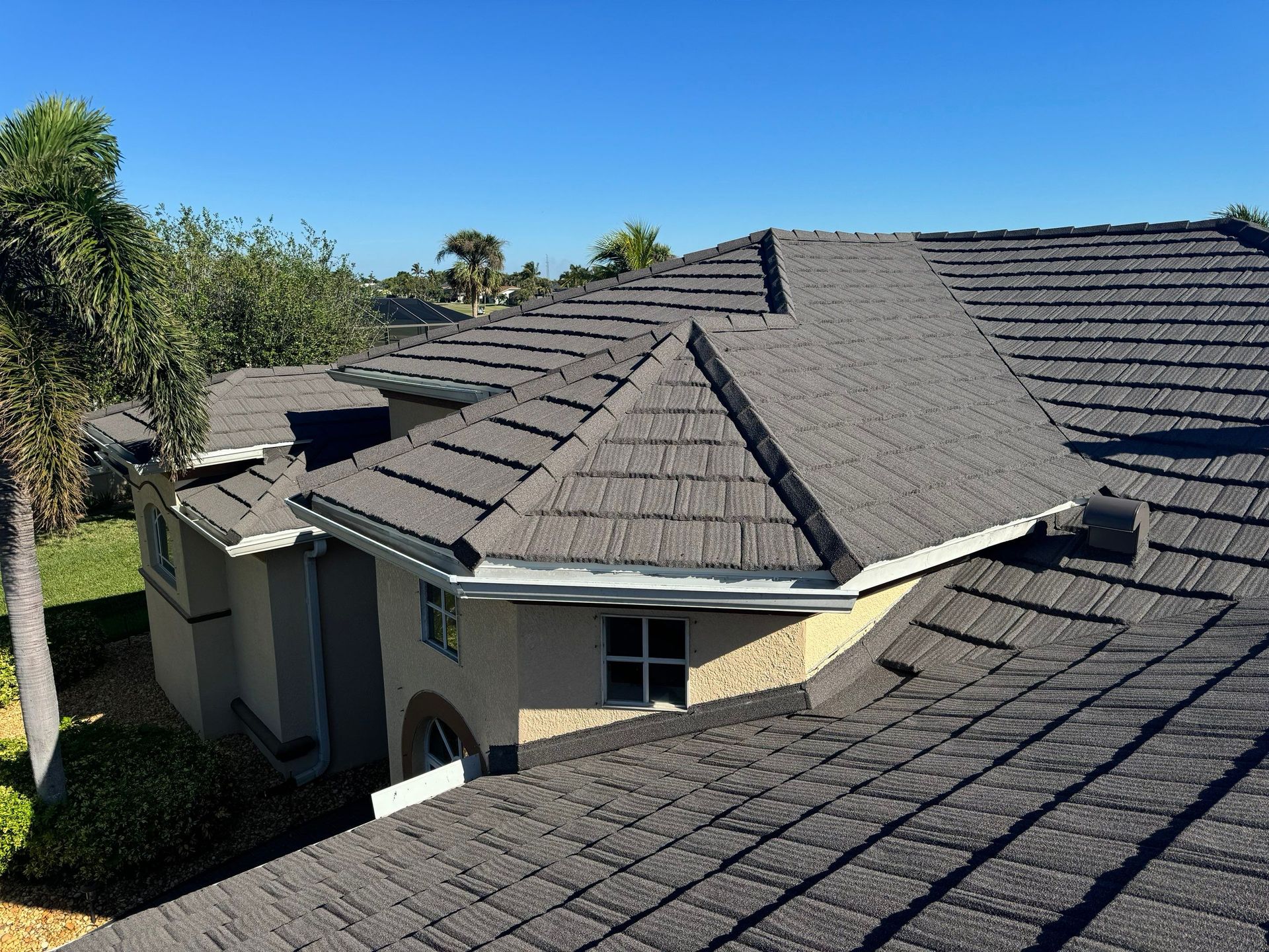 Gray tiled roof on a house under a clear blue sky.