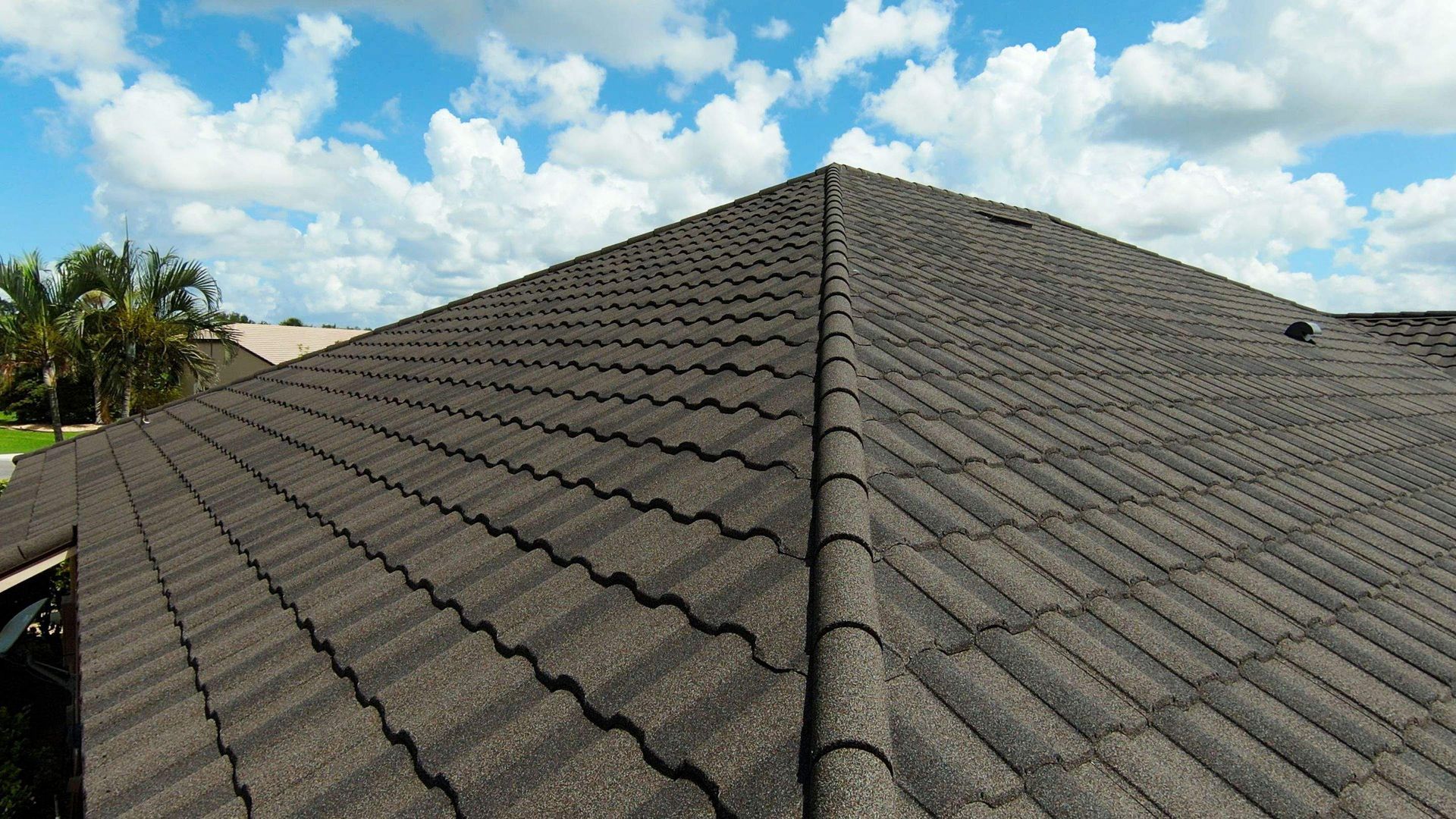 Close-up view of a brown tile roof with visible texture, under a blue sky with puffy white clouds.