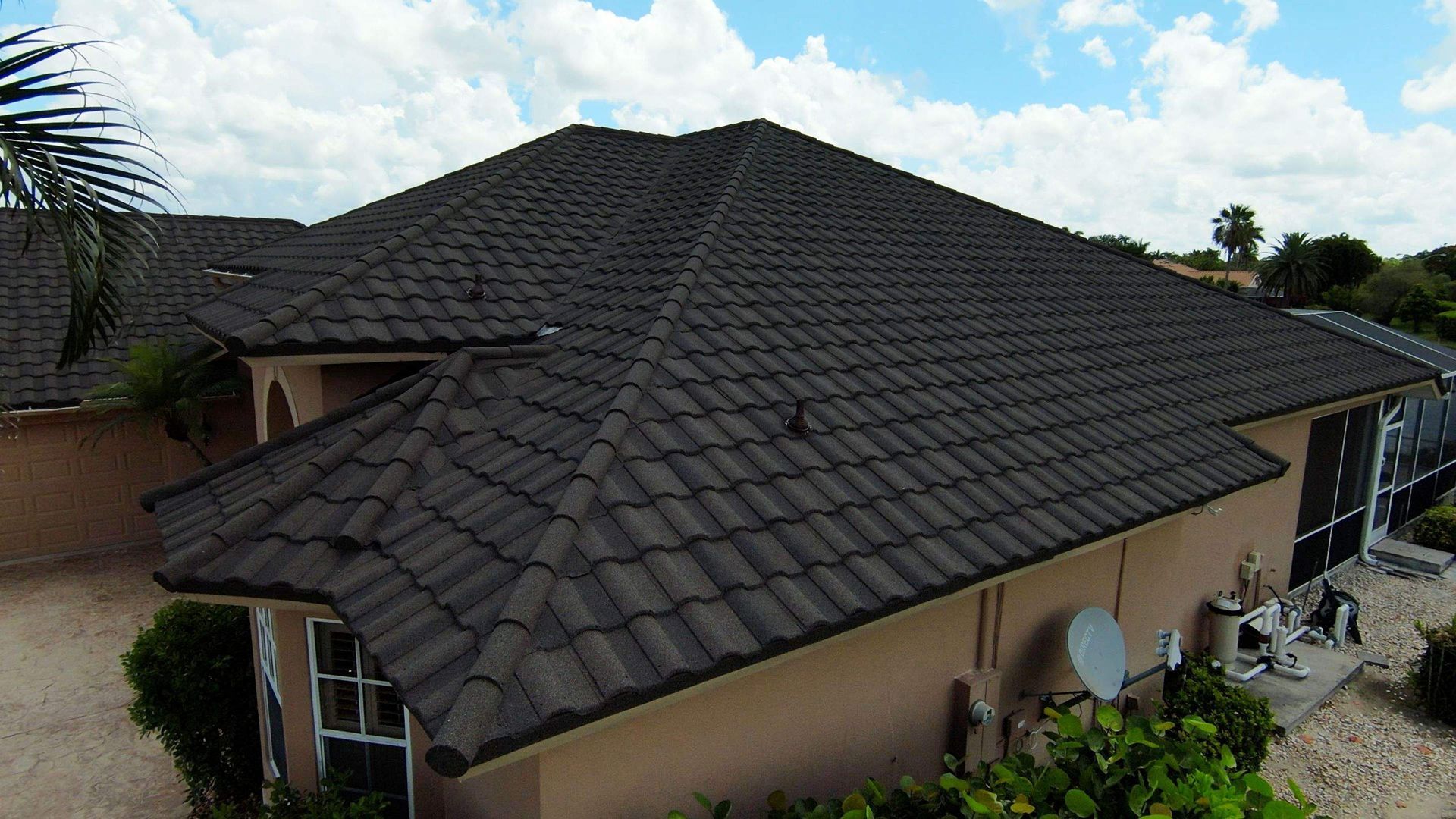 Dark tile roof on a beige house, seen from above with a partly cloudy sky.