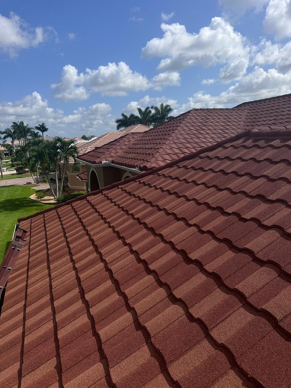 Red tiled roof on a sunny day, with a view of residential houses under a blue sky with clouds.