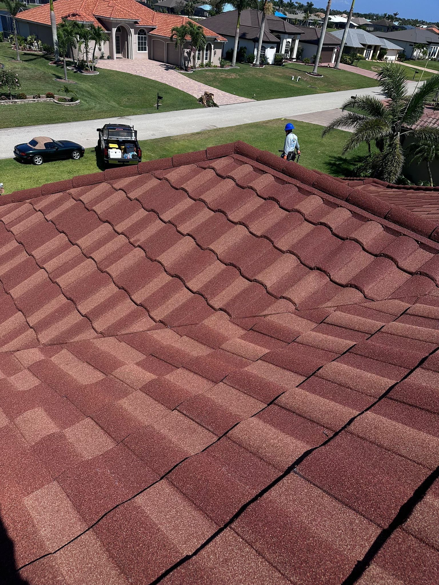 Red roof tiles with a view of neighborhood houses and vehicles on a sunny day.