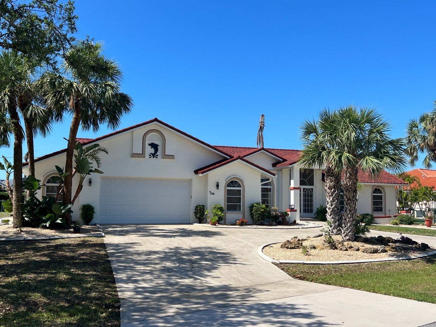 White stucco house with red-tiled roof, arched windows, and palm trees under a blue sky.