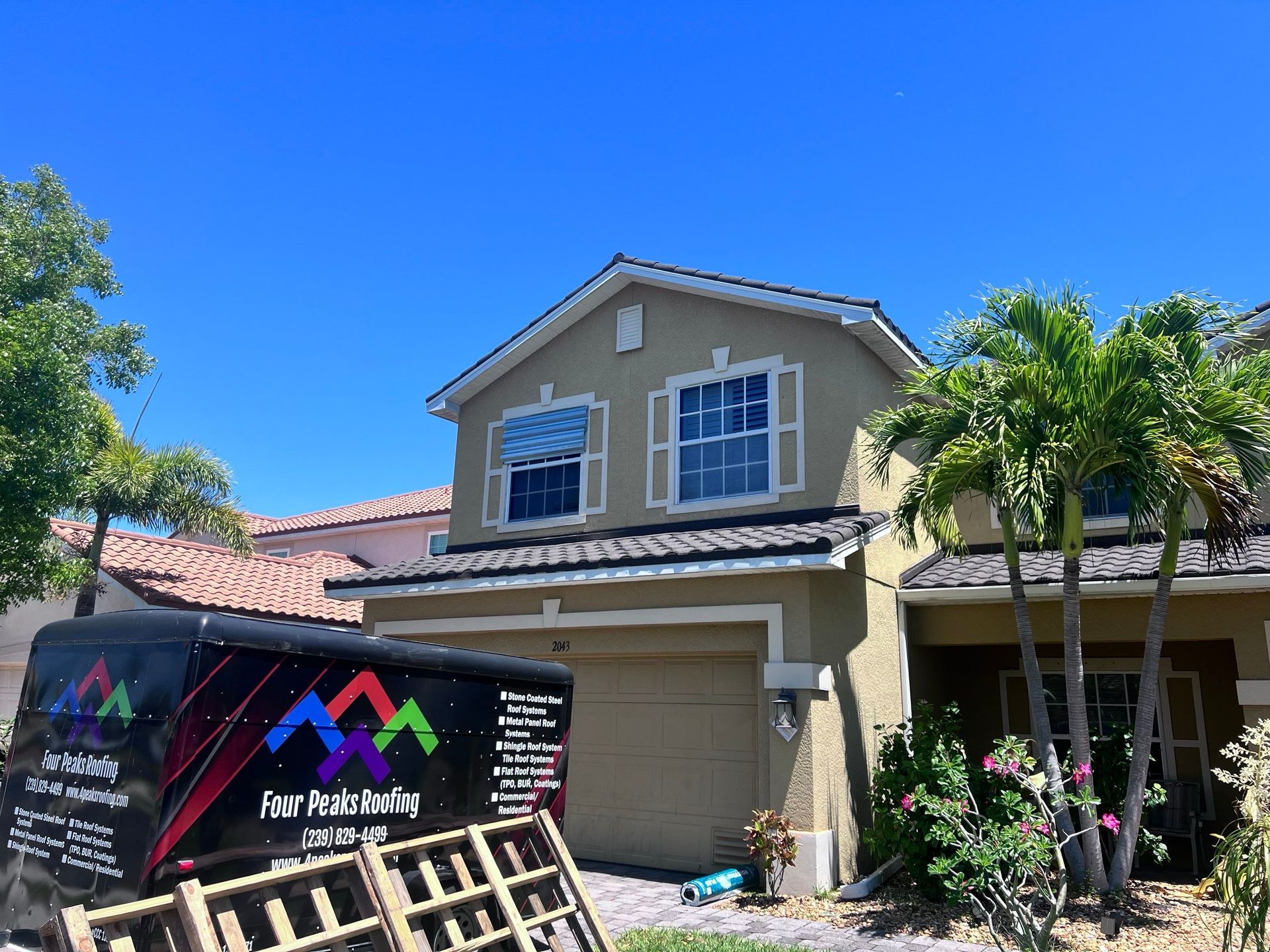 Tan house with open garage door; a company truck sits nearby under blue sky.