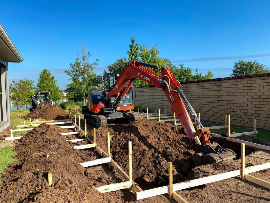 An excavator is digging a hole in the ground in front of a house.