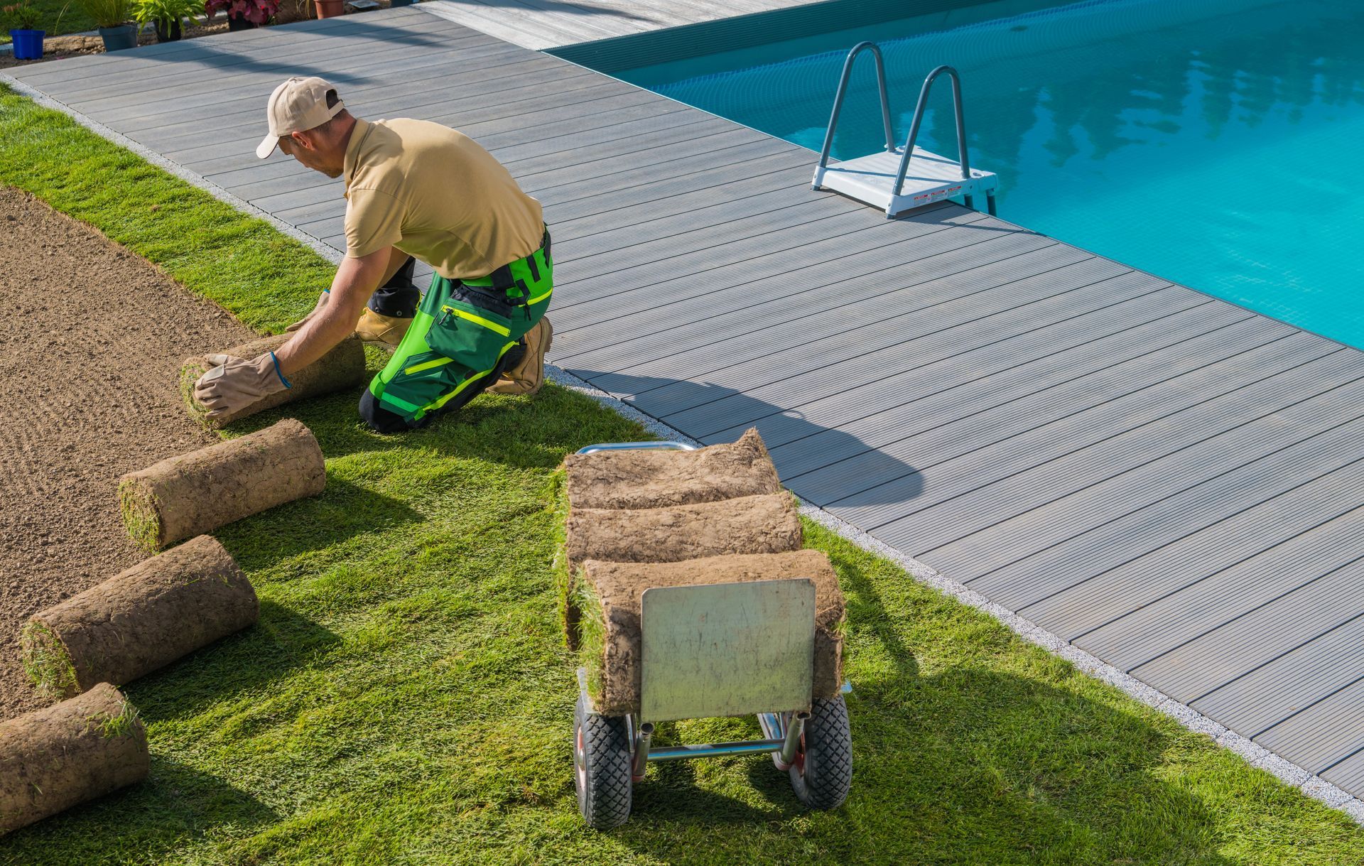 A man is laying turf next to a swimming pool.