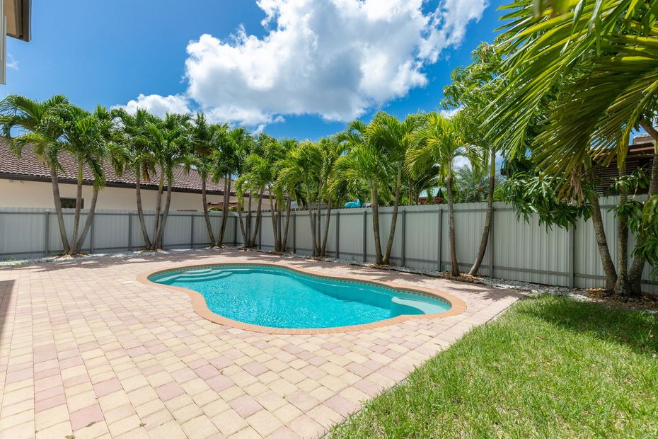 A large swimming pool is in the backyard of a house surrounded by trees.