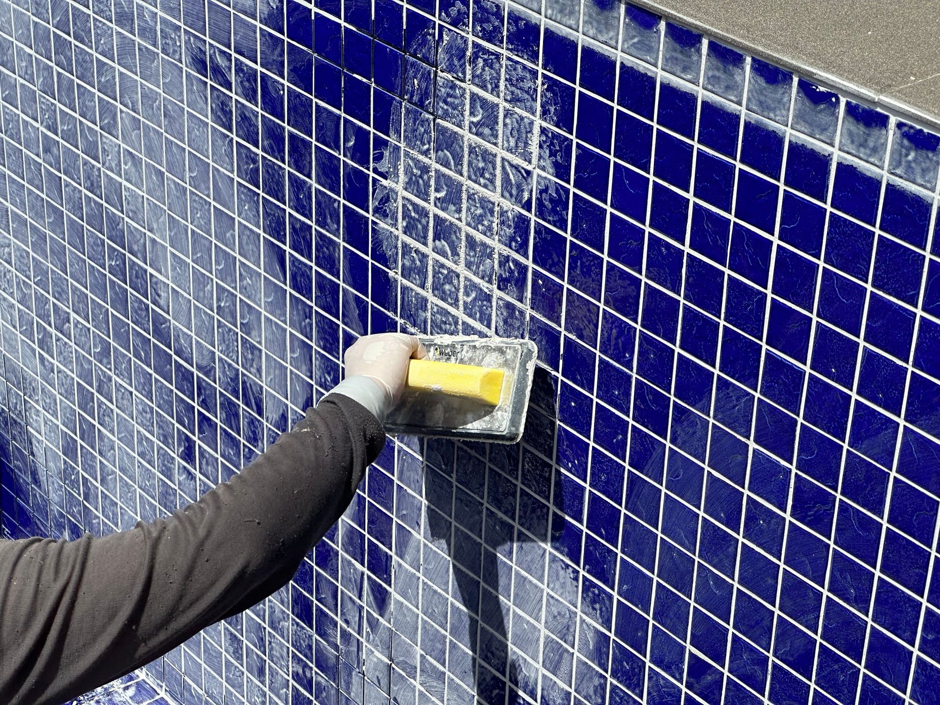 A person is cleaning a blue tiled wall with a yellow sponge.