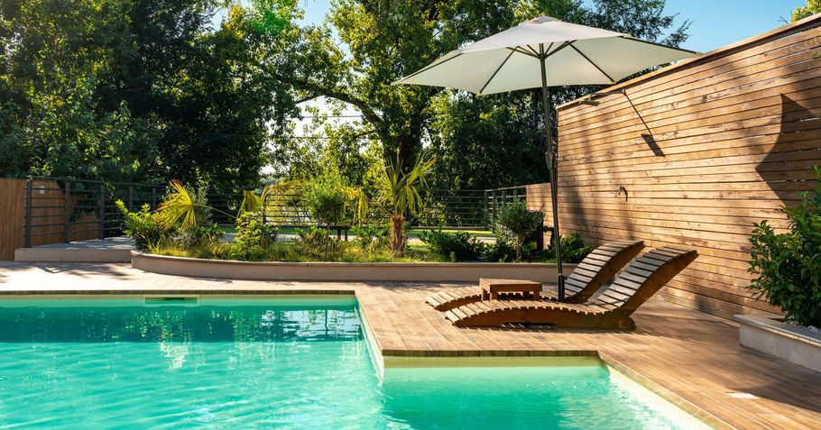 A swimming pool with a white umbrella and chairs around it.