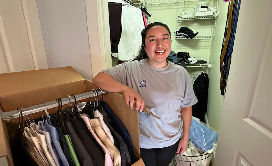 A woman is standing in a closet with clothes hanging on a rack.