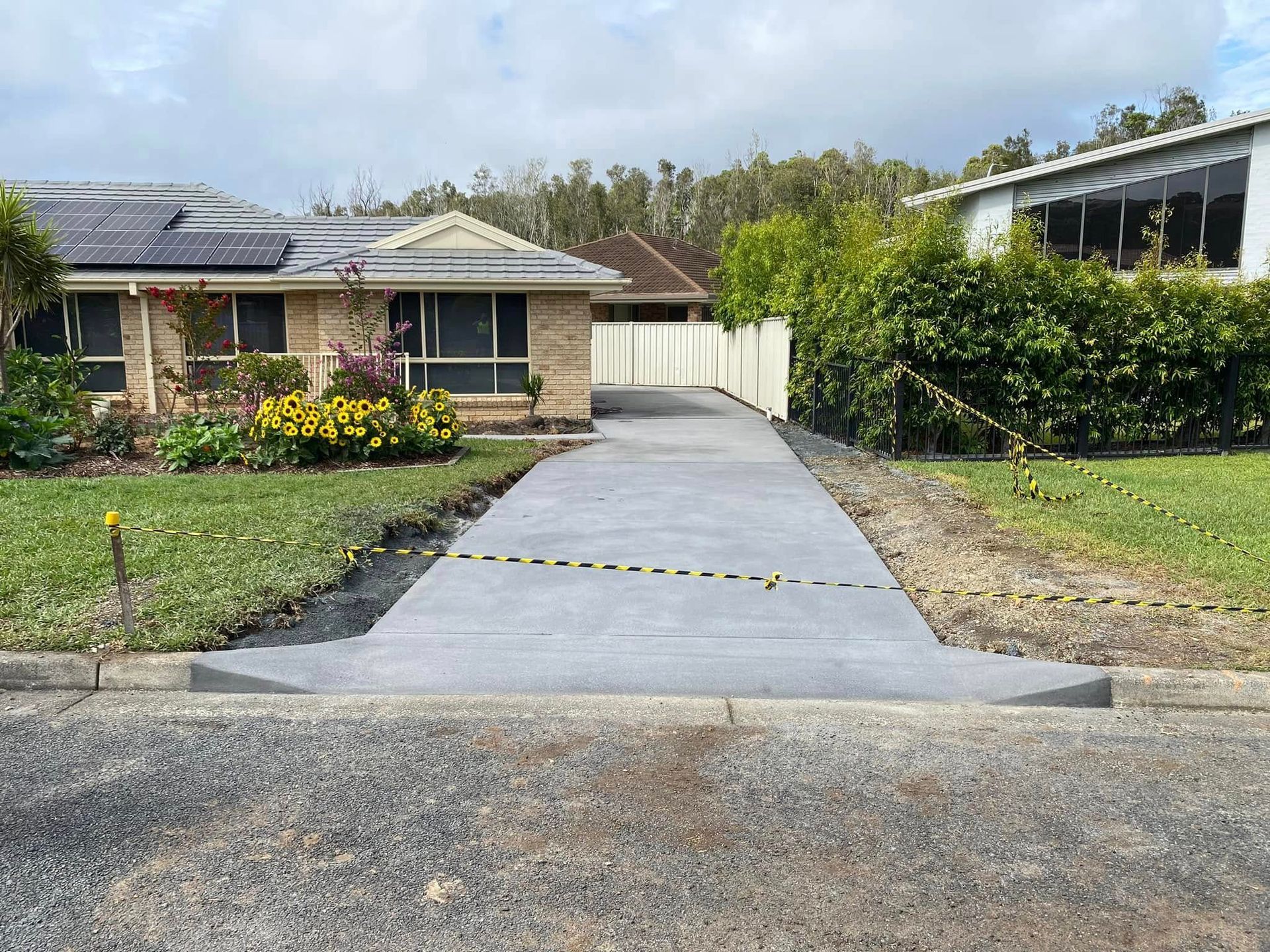 Newly Paved Gray Concrete Driveway Leading to A Suburban House with Solar Panels on The Roof — Rhyno’s Concreting In Old Bar, NSW