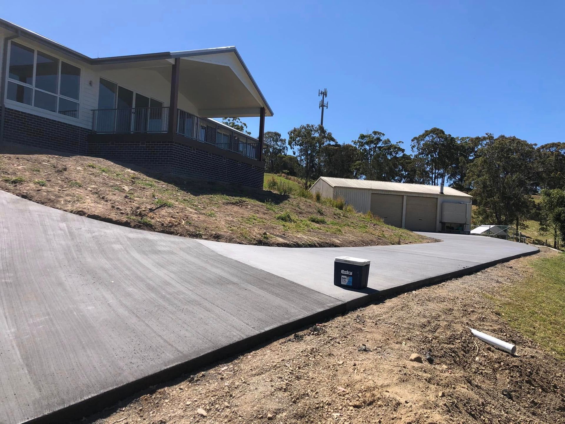 A Long, Gray Driveway Leads Uphill Towards a House on A Grassy Hill; a Garage Is in The Background — Rhyno’s Concreting In Old Bar, NSW
