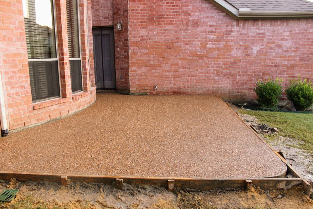 Brown concrete patio next to a red brick house with a door, window, and grass — Rhyno’s Concreting In Old Bar, NSW