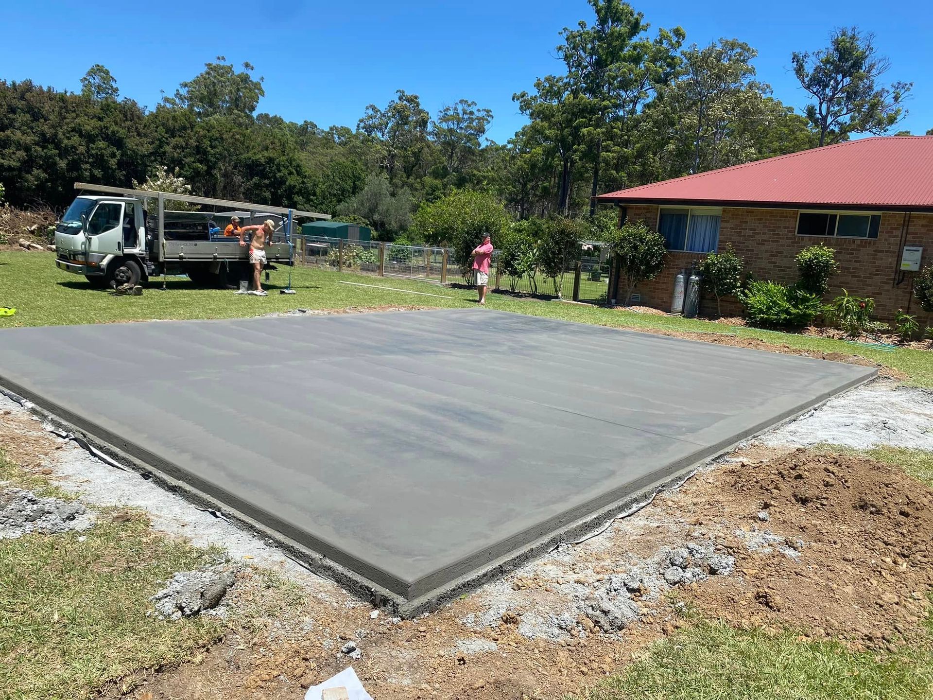 Newly Poured Concrete Slab in A Grassy Yard, with A Truck and People Nearby, Next to A House — Rhyno’s Concreting In Old Bar, NSW