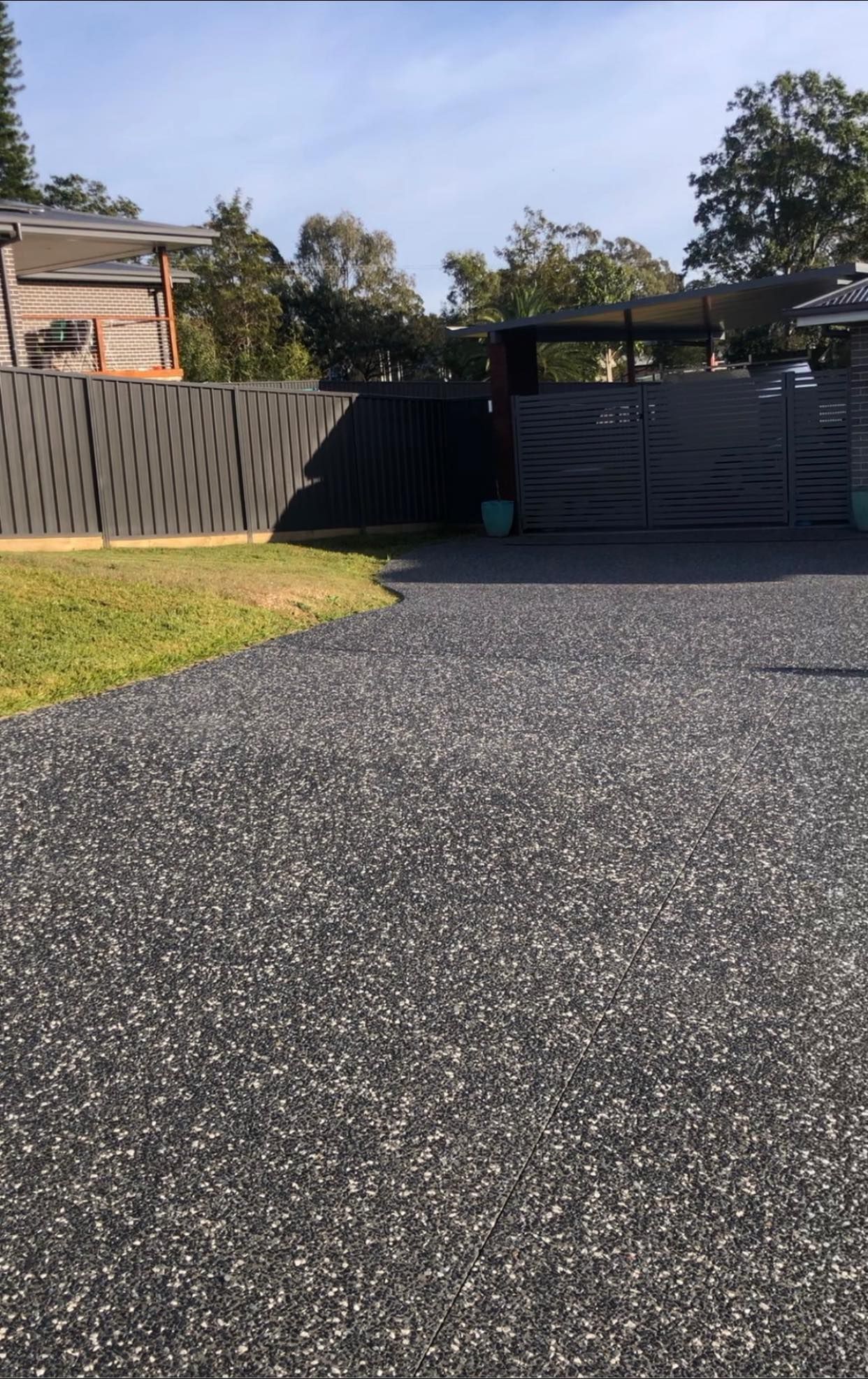 Driveway Leading to A Gated Property with A Patterned Gray Fence, Green Grass, and A Blue Sky — Rhyno’s Concreting In Old Bar, NSW