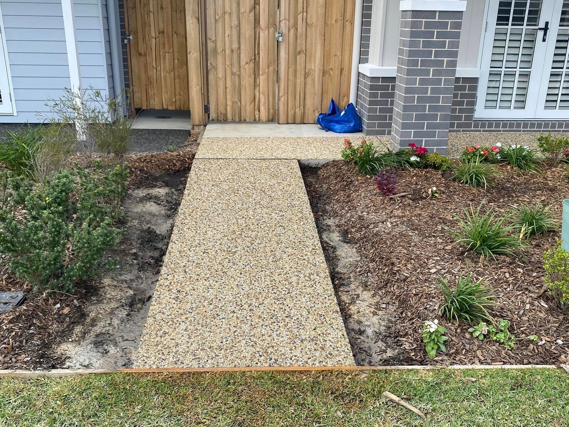 Gravel pathway leading from a lawn to a wooden gate and house entrance, bordered by mulch and plants — Rhyno’s Concreting In Old Bar, NSW