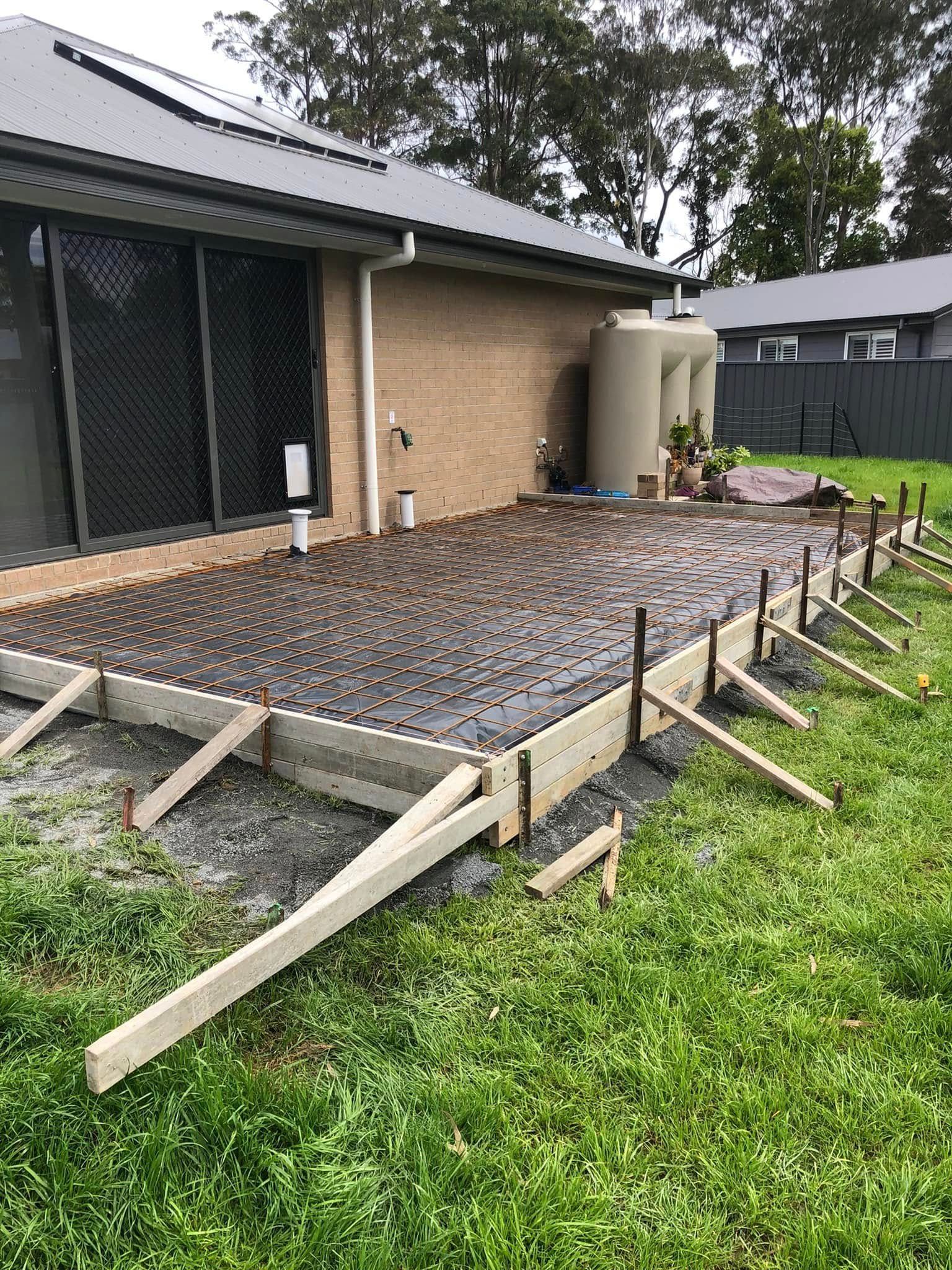 Concrete patio construction in progress next to a brick house, with wooden forms and bracing — Rhyno’s Concreting In Old Bar, NSW