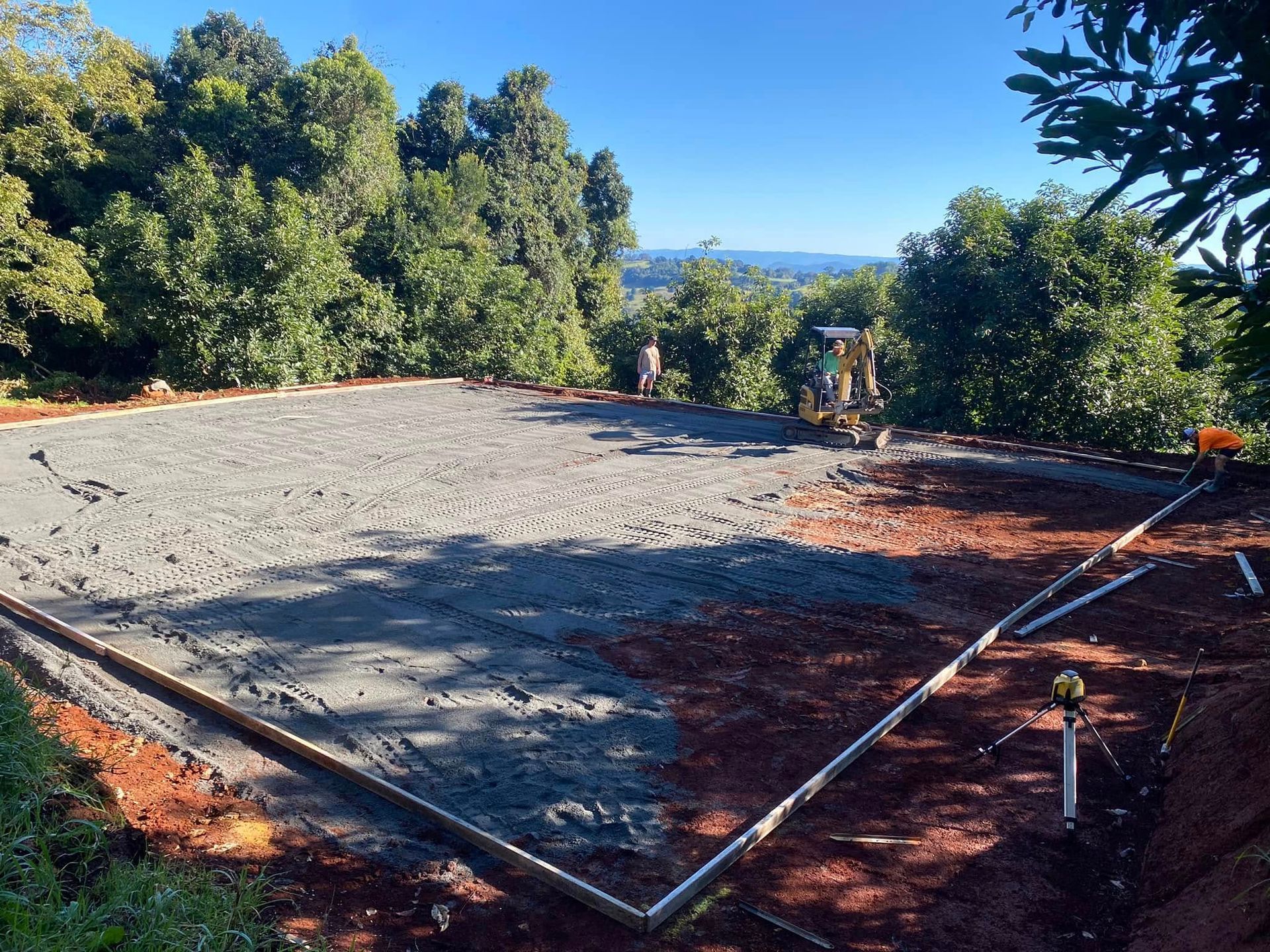 Construction Site with Fresh Concrete Slab, Surrounded by Red Soil, Trees, and An Excavator. Sunny Day — Rhyno’s Concreting In Old Bar, NSW