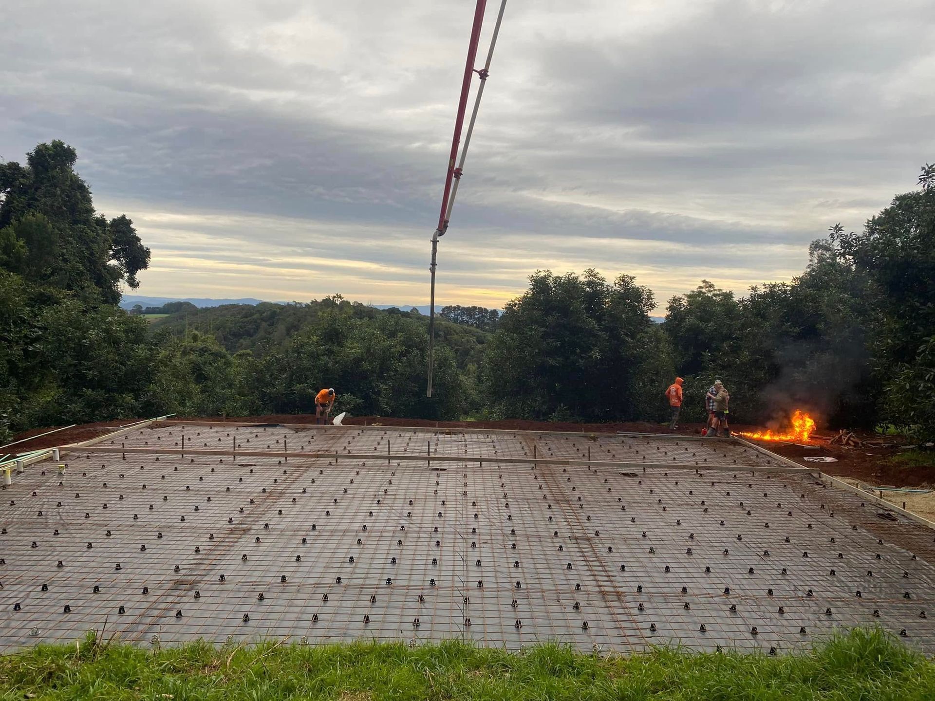 Concrete Pour in Progress. Workers at A Construction Site with Trees and Overcast Sky in The Background, Fire Burning — Rhyno’s Concreting In Old Bar, NSW