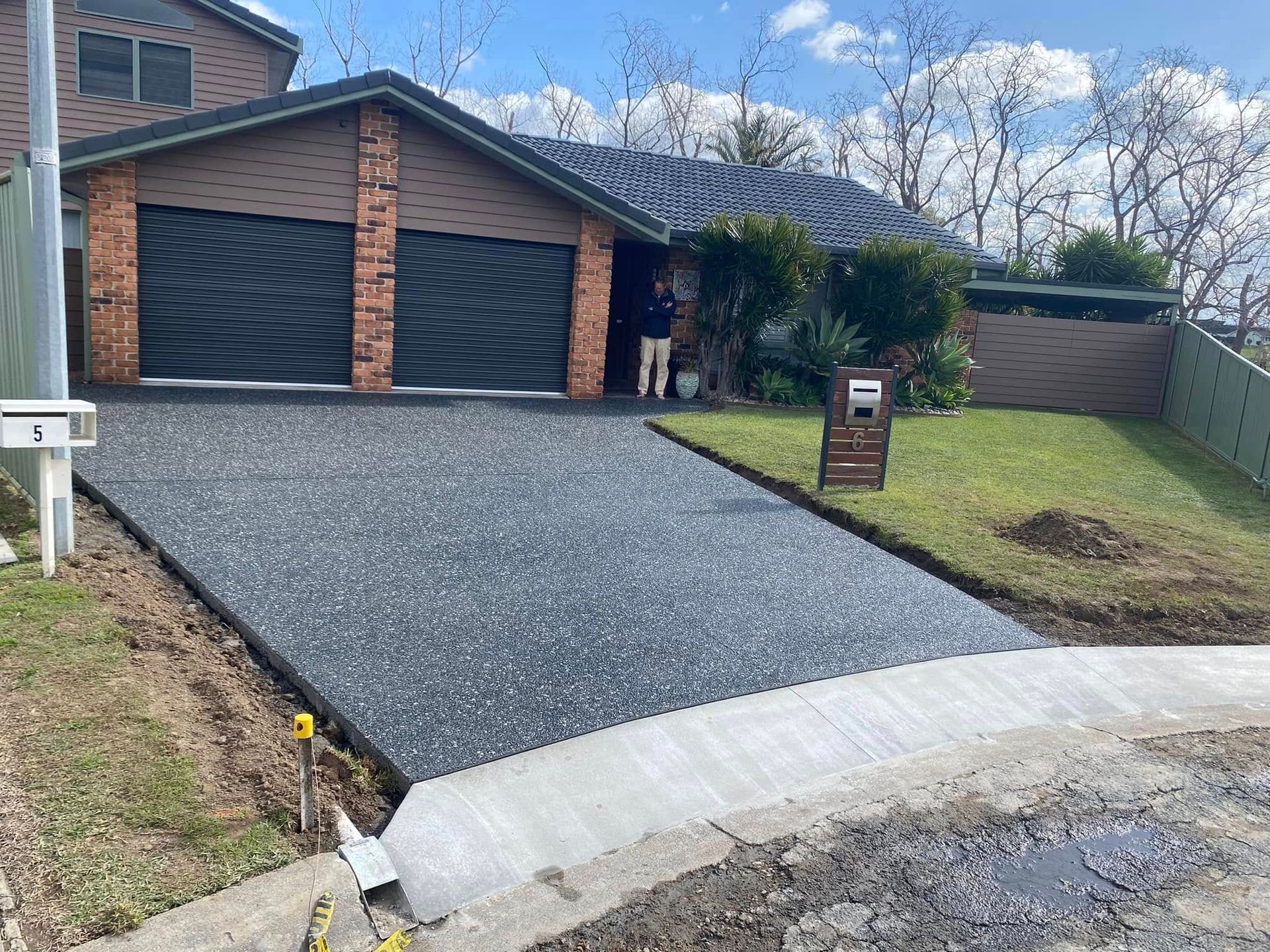 Driveway with A Dark, Textured Surface, Next to A House with Brick and A Garage — Rhyno’s Concreting In Old Bar, NSW