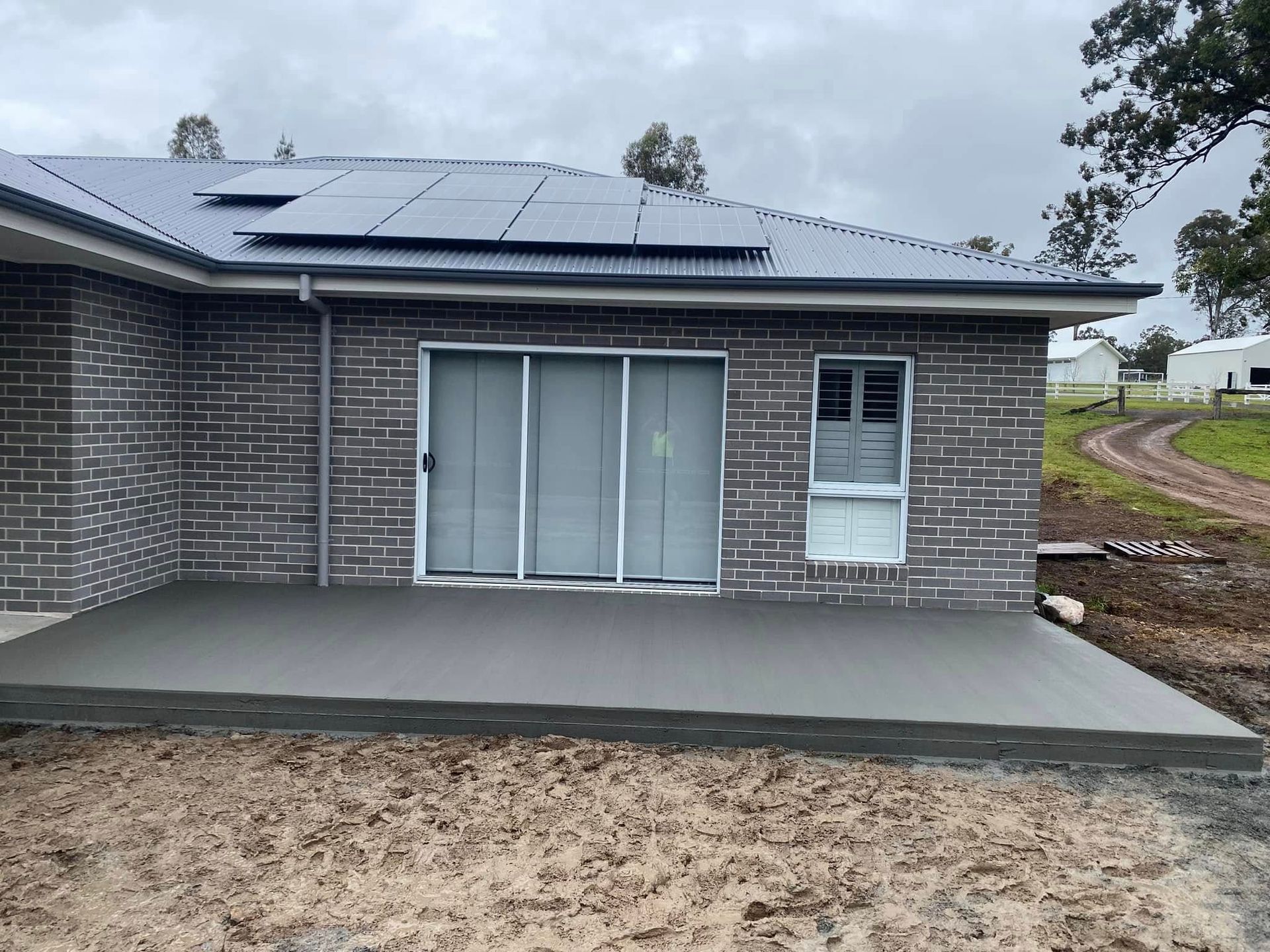 Newly Poured Concrete Patio Outside a Brick Home with Sliding Doors and A Window. Cloudy Day — Rhyno’s Concreting In Old Bar, NSW