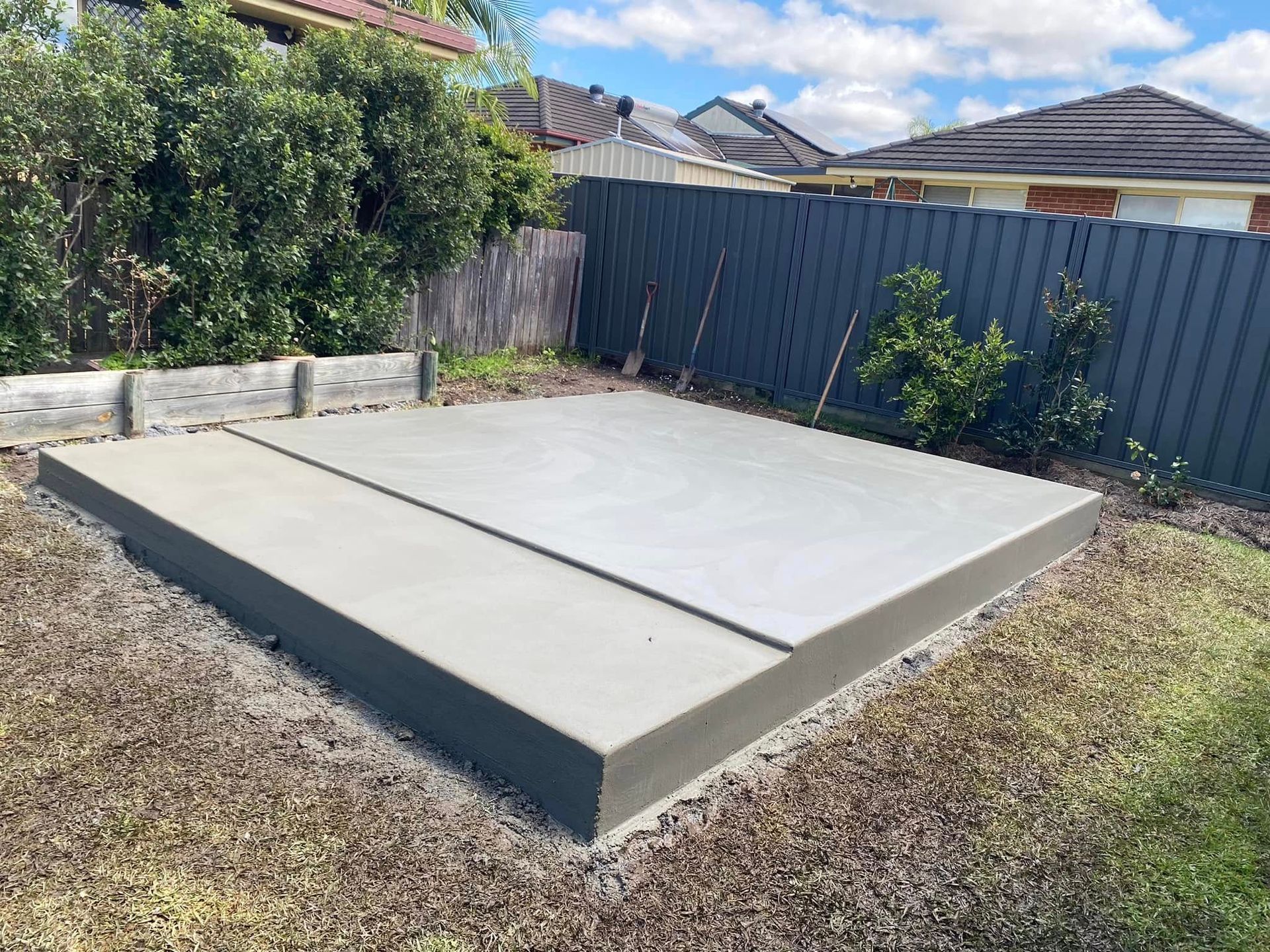 Concrete slab in a backyard with a dark grey fence and surrounding foliage — Rhyno’s Concreting In Old Bar, NSW