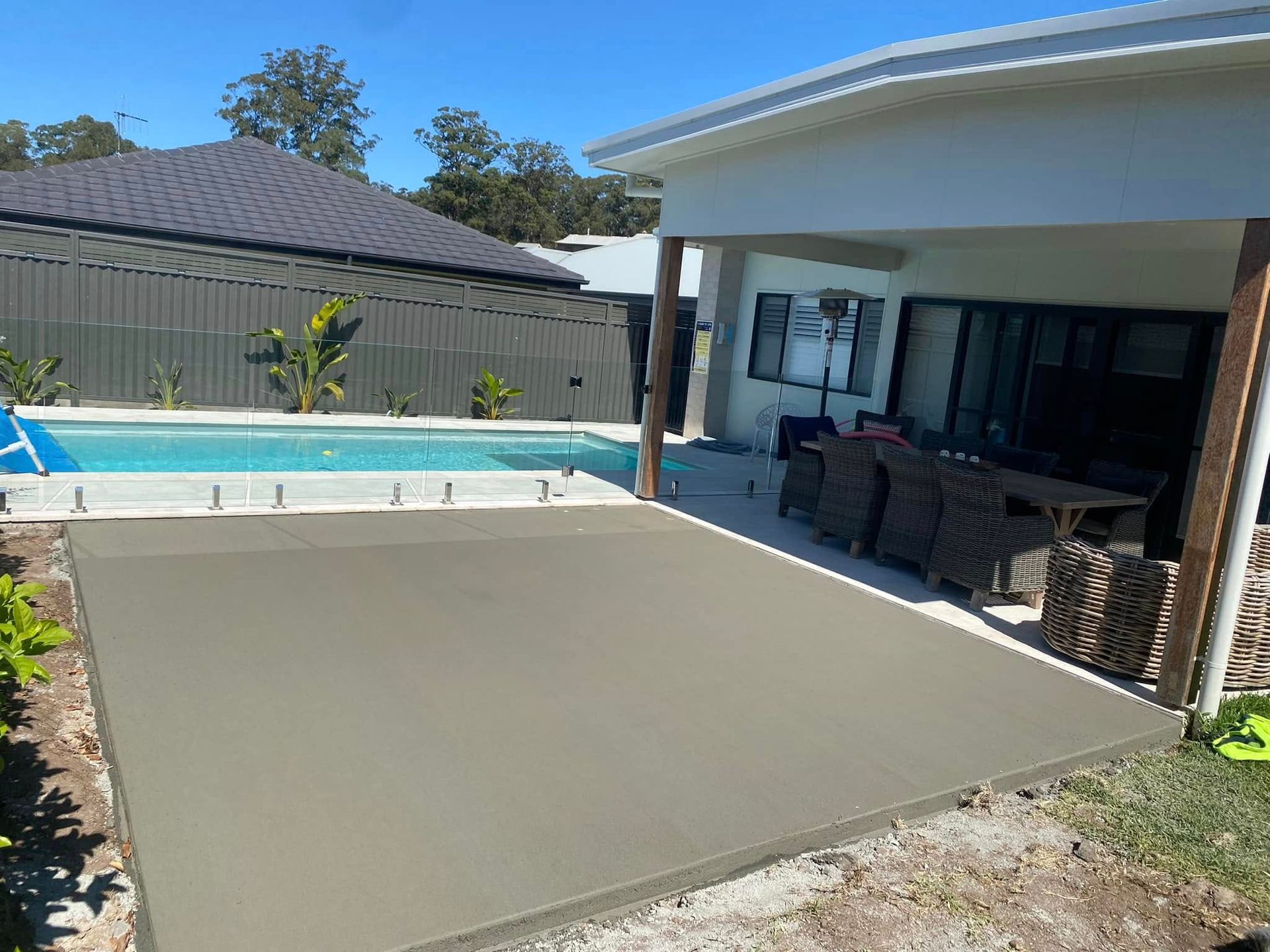 Newly poured concrete patio next to a swimming pool, adjacent to a house with outdoor furniture — Rhyno’s Concreting In Old Bar, NSW