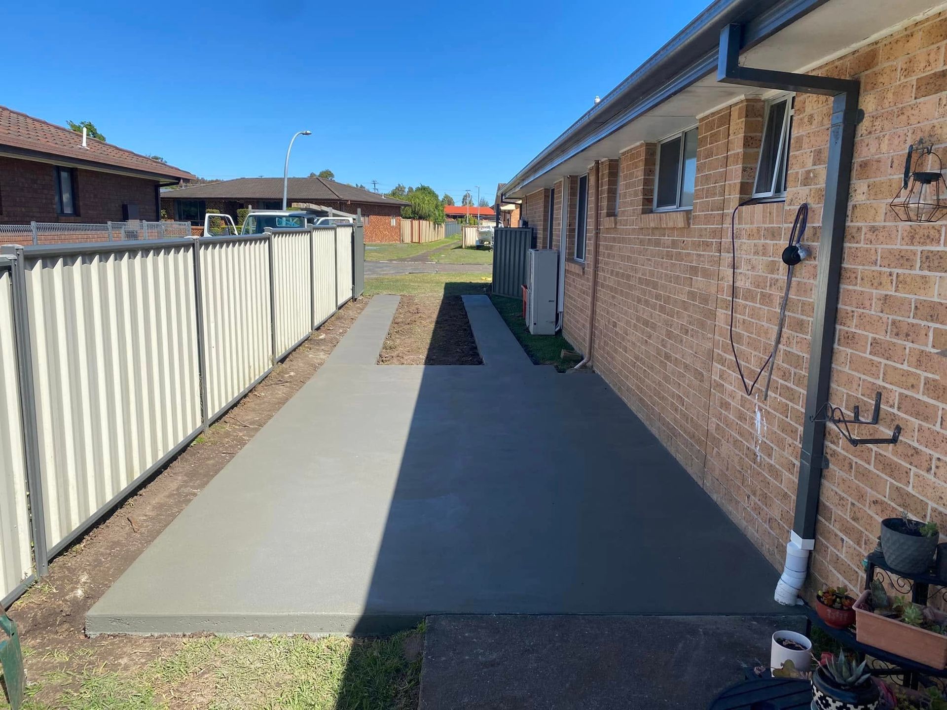 Concrete pathway next to brick building and a white fence, sunny day — Rhyno’s Concreting In Old Bar, NSW