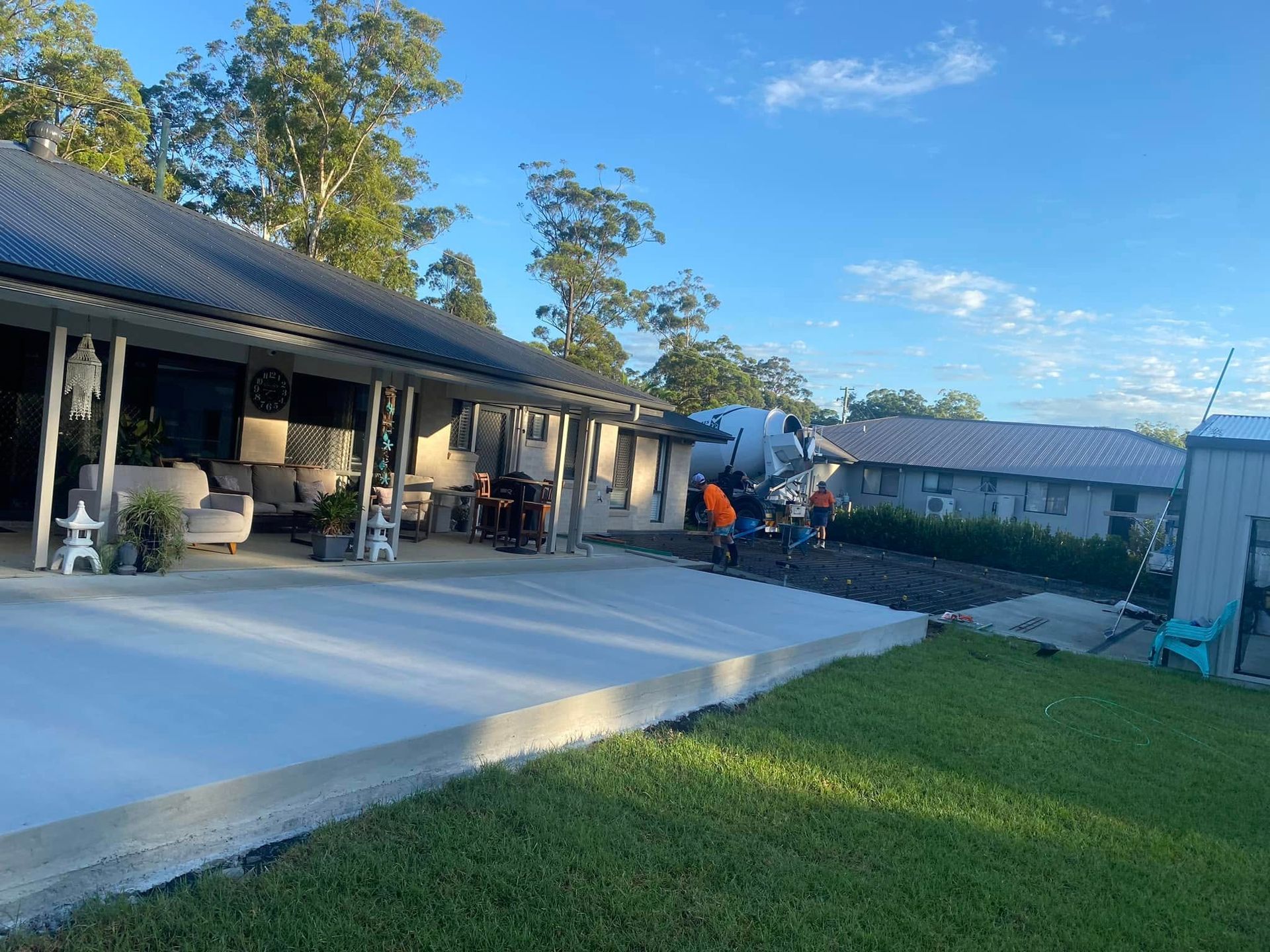 A concrete patio in front of a house, with workers unloading equipment. Sunny day, green grass — Rhyno’s Concreting In Old Bar, NSW