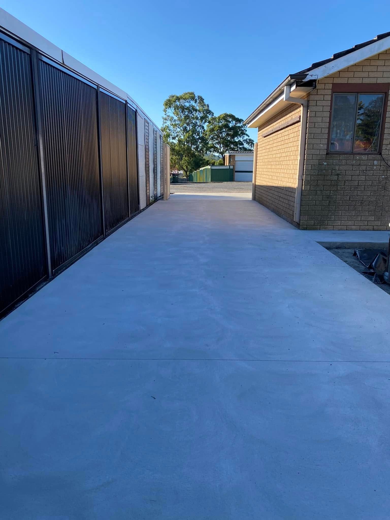Concrete driveway between a black fence and a brick house — Rhyno’s Concreting In Old Bar, NSW