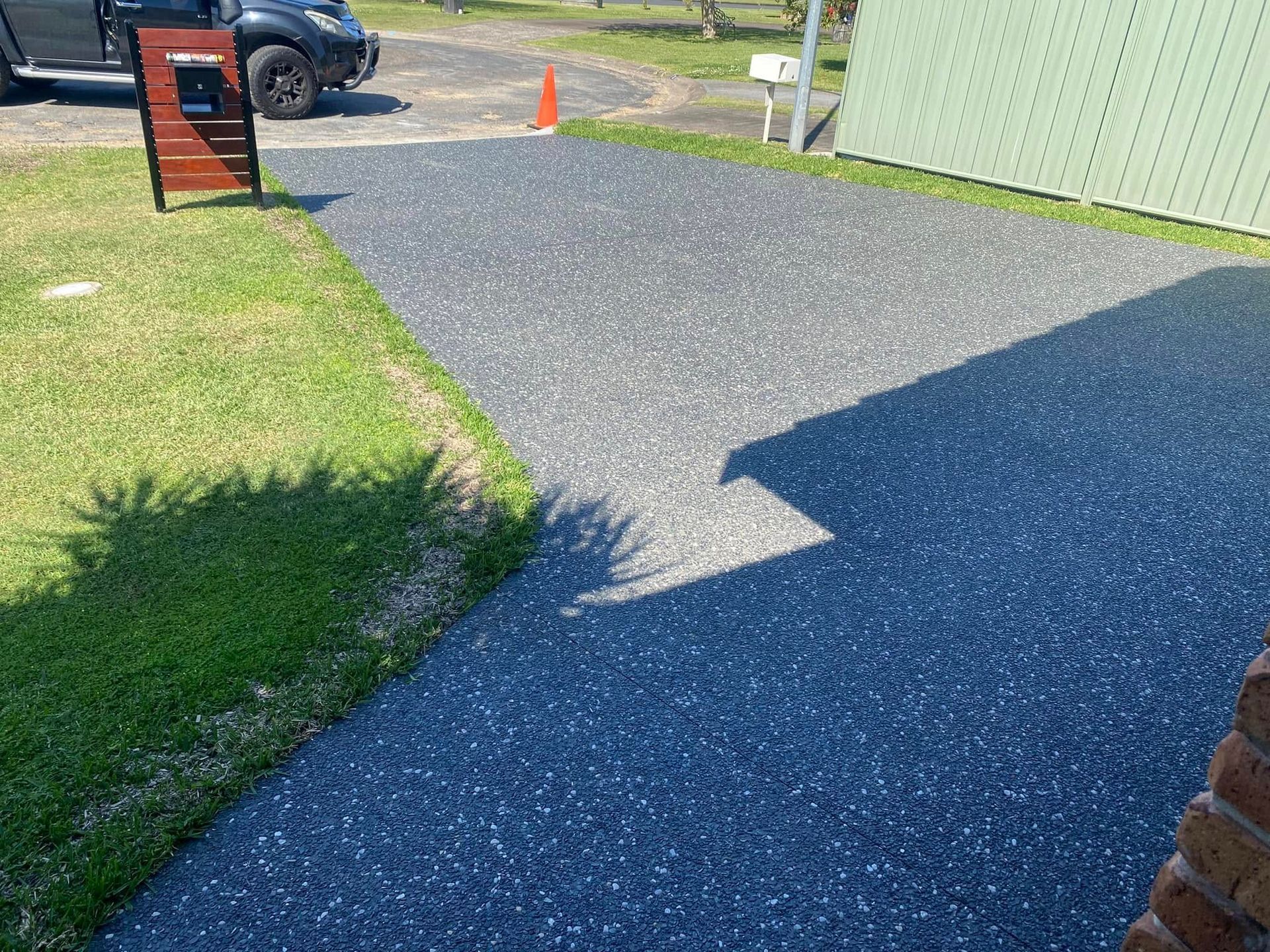 Dark grey speckled driveway with green grass and black parked car — Rhyno’s Concreting In Old Bar, NSW