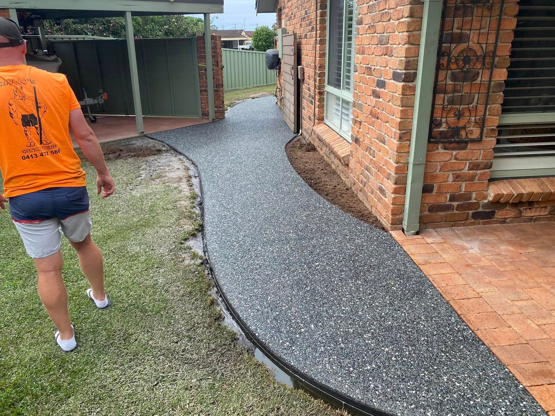Man Walks Along a Gravel Pathway Next to a Brick Building — Rhyno’s Concreting In Old Bar, NSW