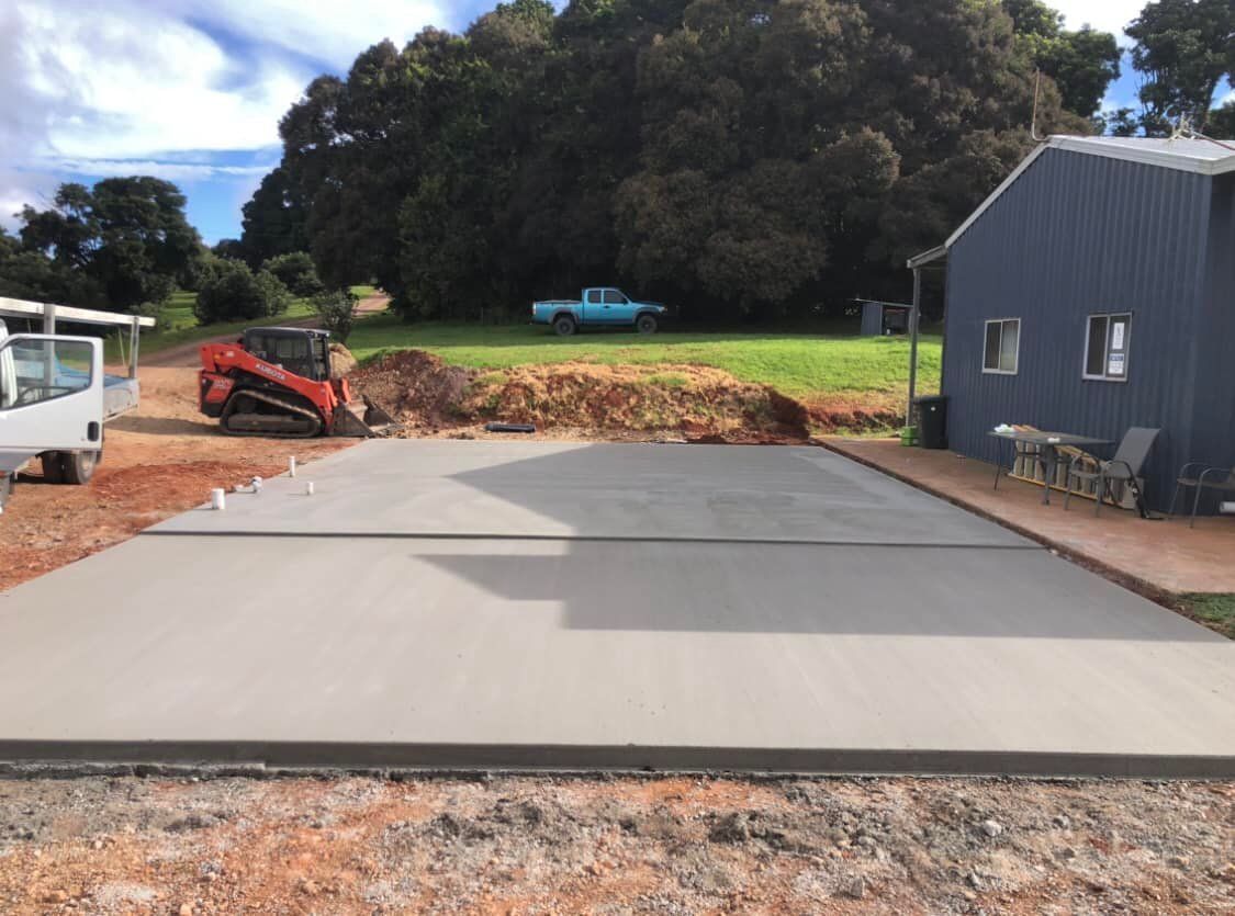 Newly Poured Concrete Slab; Small Excavator, Blue Truck, and Shed in Background — Rhyno’s Concreting In Old Bar, NSW