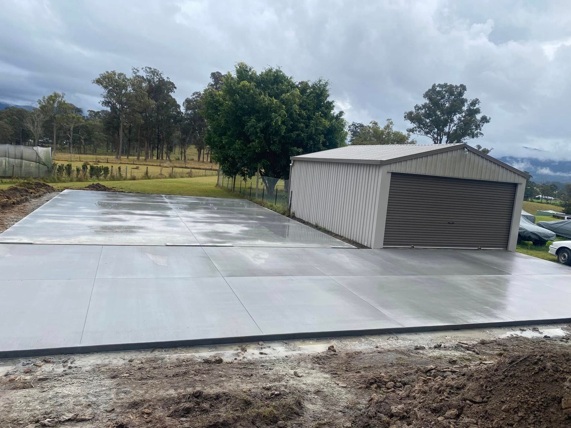 Newly poured concrete slab with a metal shed under a cloudy sky — Rhyno’s Concreting In Old Bar, NSW