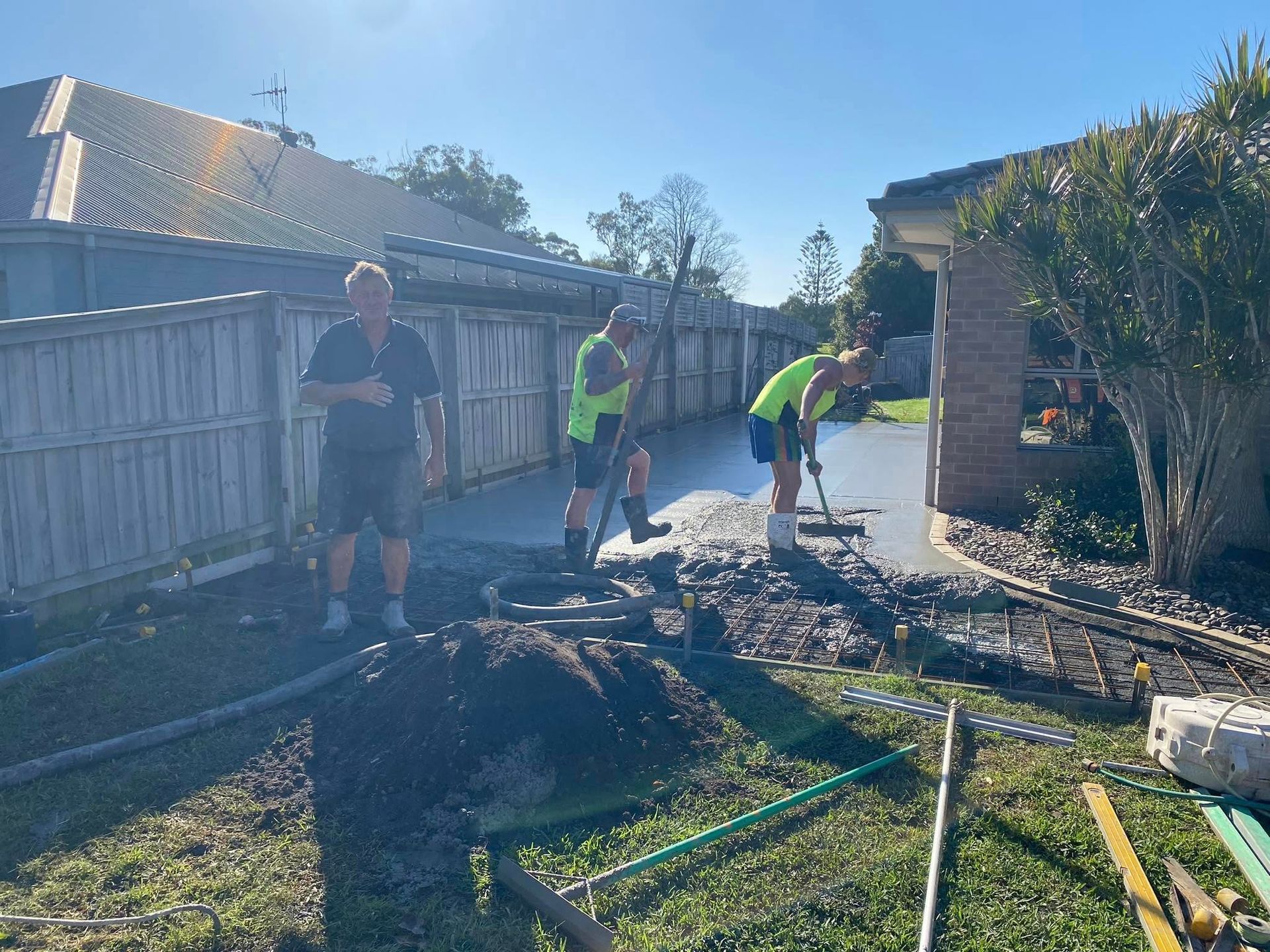 Three Workers Pouring Concrete in A Backyard Next to A House. One Is Watching, Two Are Working with The Concrete — Rhyno’s Concreting In Old Bar, NSW