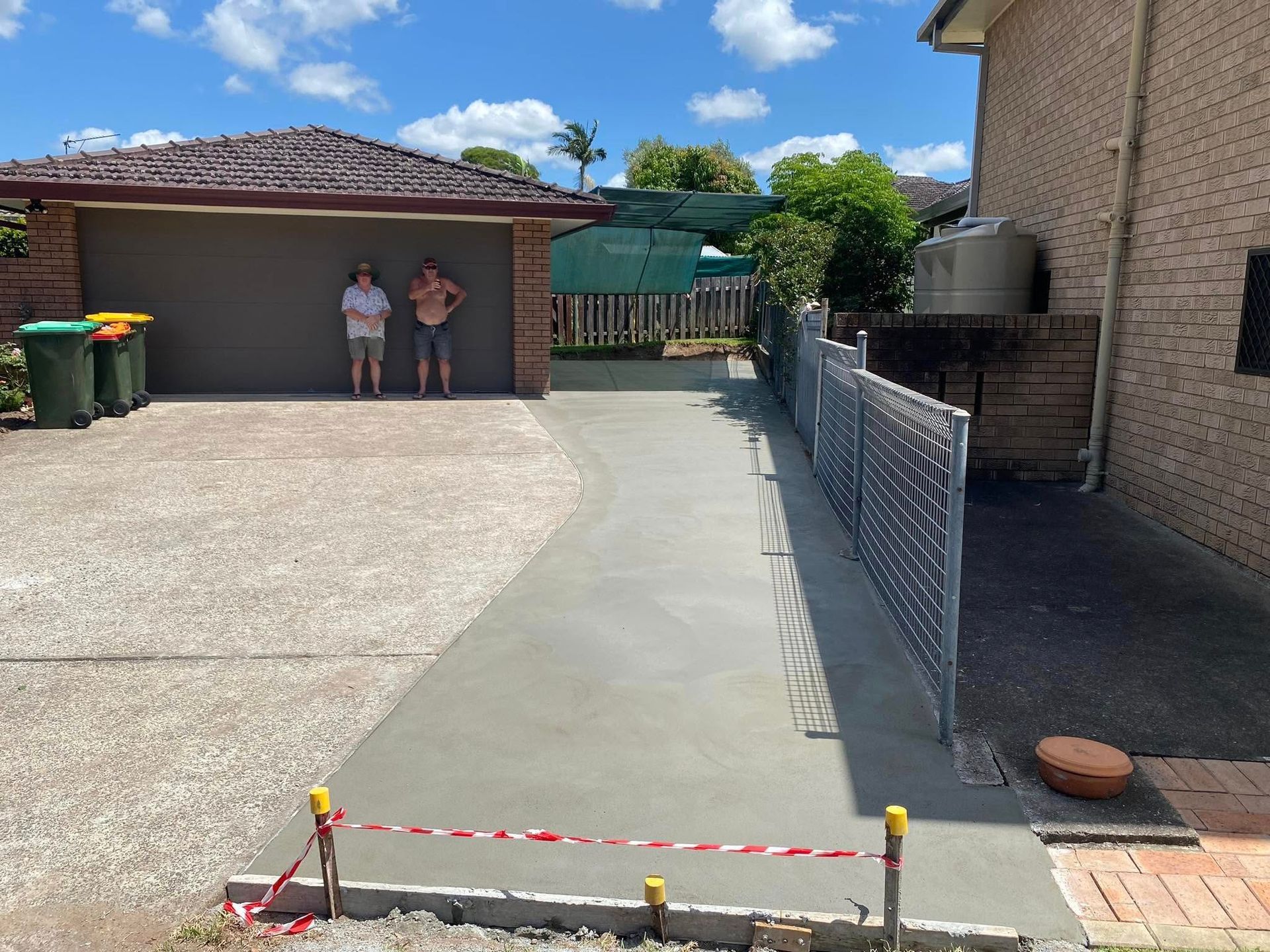 Freshly poured concrete driveway with a garage on the left and a metal fence on the right — Rhyno’s Concreting In Old Bar, NSW