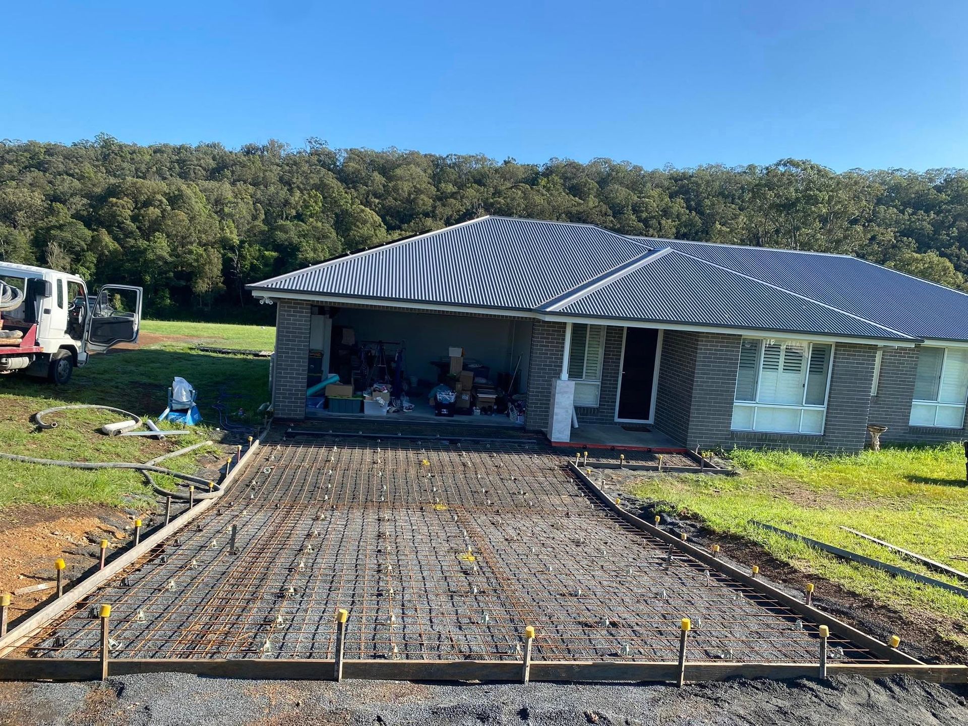 Concrete Driveway Under Construction in Front of A House, with Reinforcement Bars Visible, Surrounded by Grass and Trees — Rhyno’s Concreting In Old Bar, NSW
