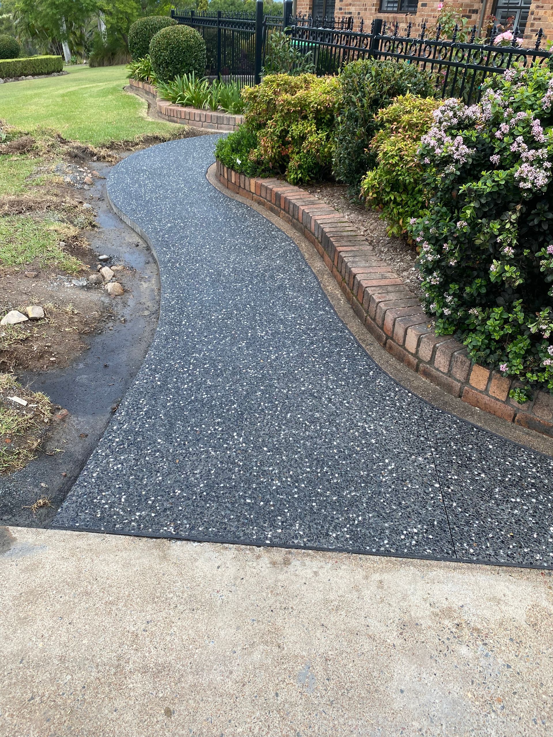 Curved gravel garden path beside a brick-edged flower bed and green lawn
