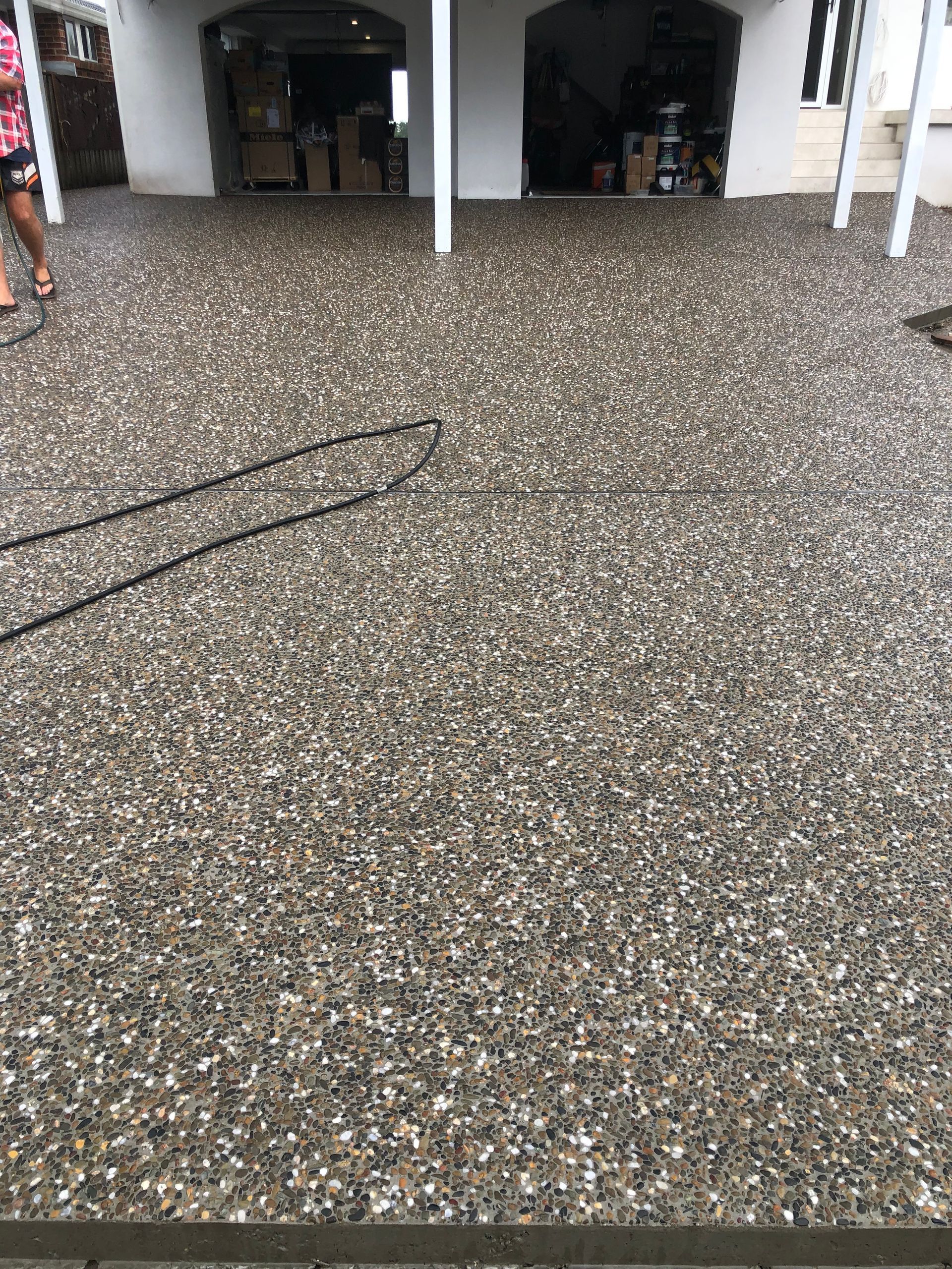 Speckled concrete floor in a covered outdoor area with open doorways and a black cable on the ground
