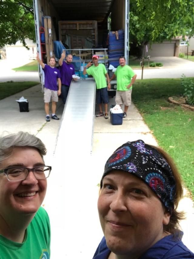 Group of movers with a ramp, assisting two women taking a selfie in a driveway