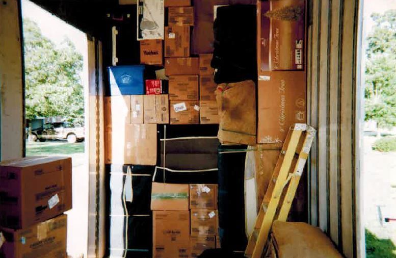 Boxes stacked inside a storage unit, door open with a view of trees and a vehicle